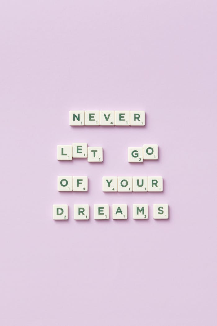 Letter tiles spell 'Never let go of your dreams' on a pastel purple background.